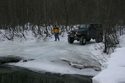 2003 Jeep TJ - A dark blue 2003 Jeep TJ navigates a slippery, icy road in a wooded area during winter.