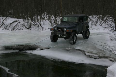 2003 Jeep TJ - A Jeep TJ navigates a frozen river in a snowy, wooded area during winter.