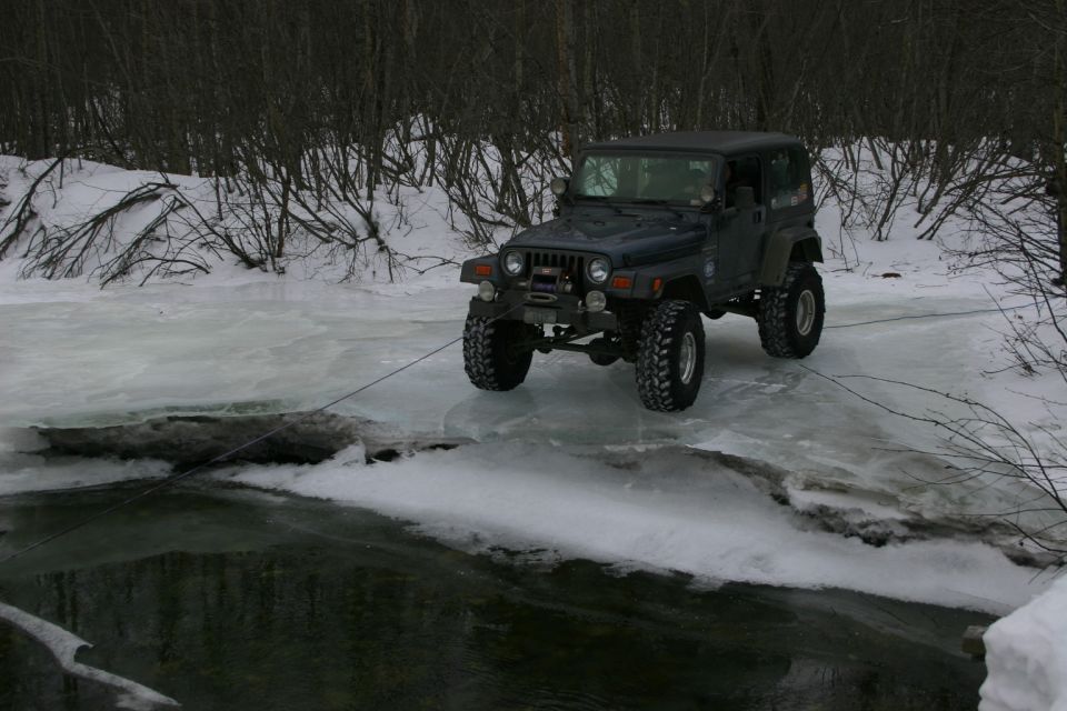 Dark green Jeep TJ with winch on icy river, winter scene