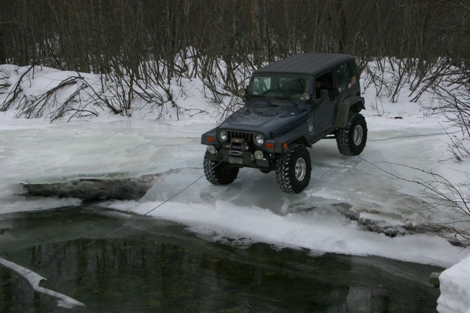 Dark blue Jeep TJ on ice near water, with a winch cable attached