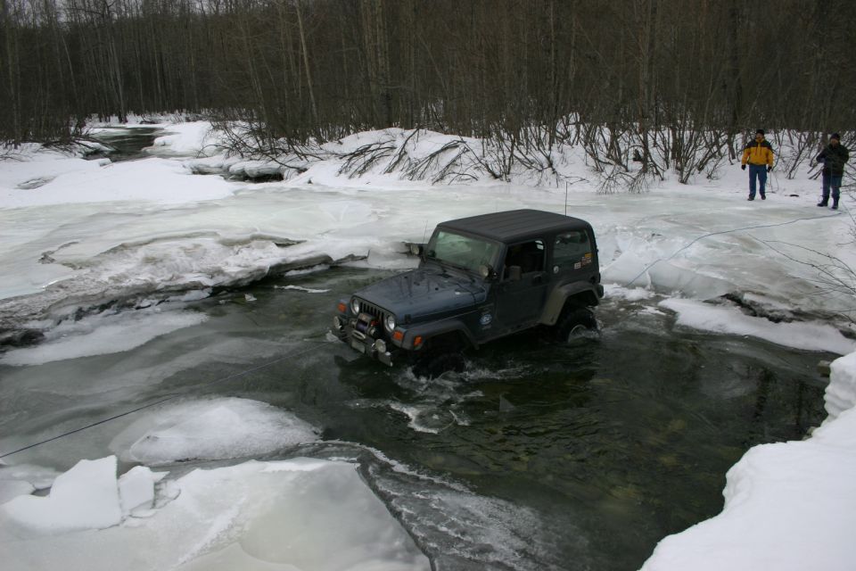 Dark blue 2003 Jeep TJ driving through icy water with two people watching