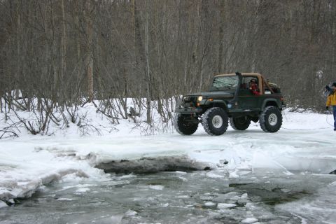 2003 Jeep TJ - A green 2003 Jeep TJ navigates an icy path through a wooded area during winter.