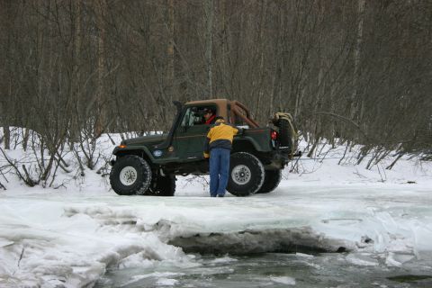 2003 Jeep TJ - A modified 2003 Jeep TJ navigates a snowy and icy terrain with a person standing near the rear.