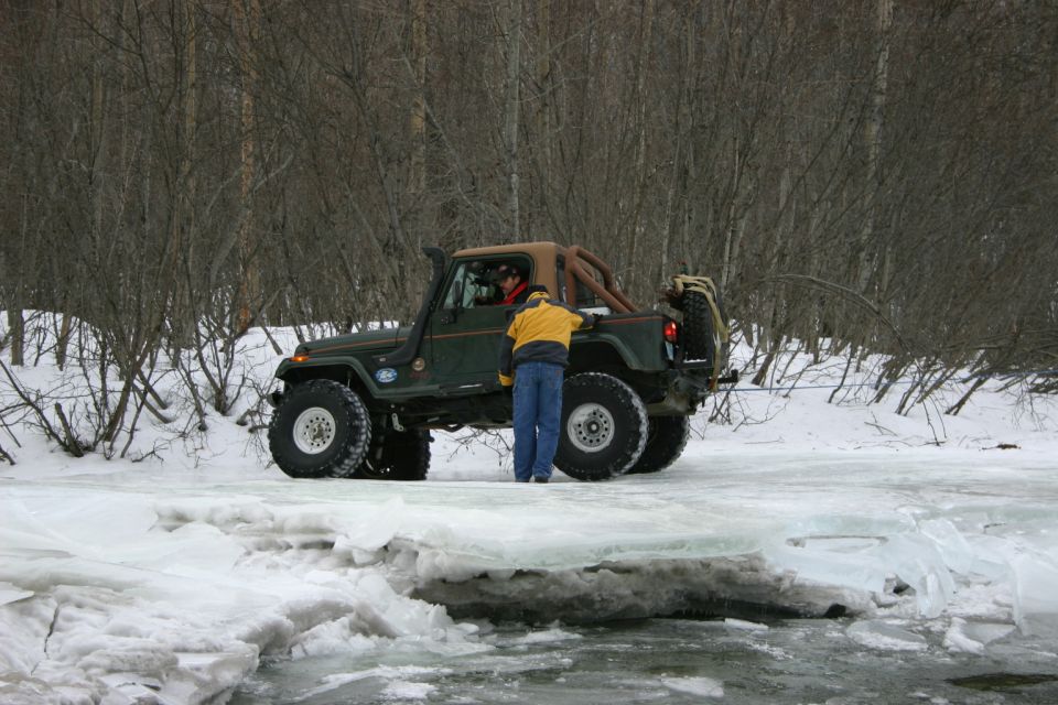 Green 2003 Jeep TJ with snorkel and large tires driving on ice and snow