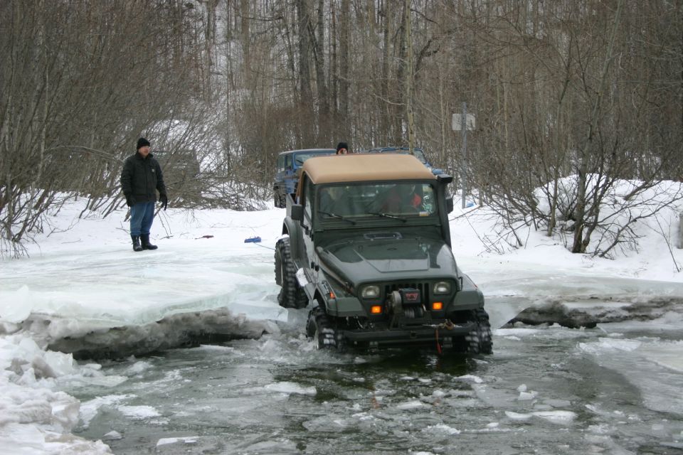 Green 2003 Jeep TJ driving through icy water with another Jeep behind it. A person stands on the ice bank