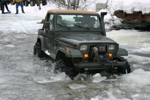 2003 Jeep TJ - A green Jeep Wrangler navigates through icy water, demonstrating its off-road capabilities.