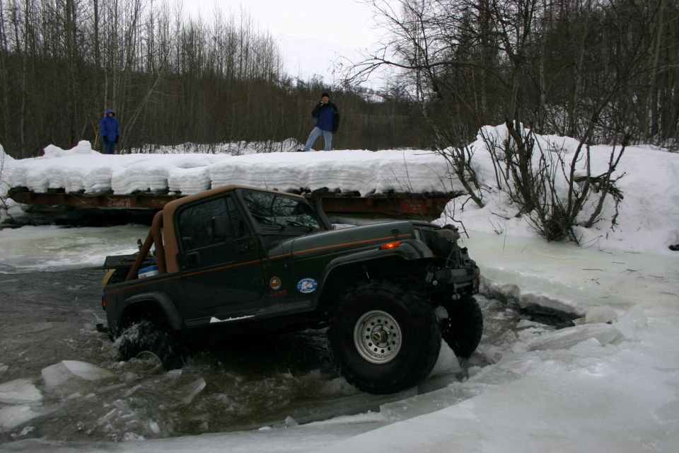 Green 2003 Jeep TJ driving through icy water with snow on the banks