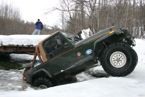 2003 Jeep TJ - A green Jeep TJ Wrangler navigates through a snowy and icy terrain, with a person observing from a bridge above.