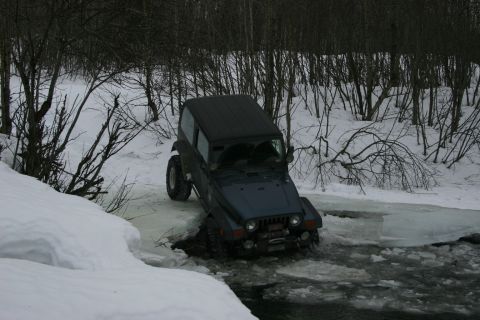 2003 Jeep TJ - A dark blue Jeep Wrangler TJ navigates through icy water in a snowy, wooded environment.
