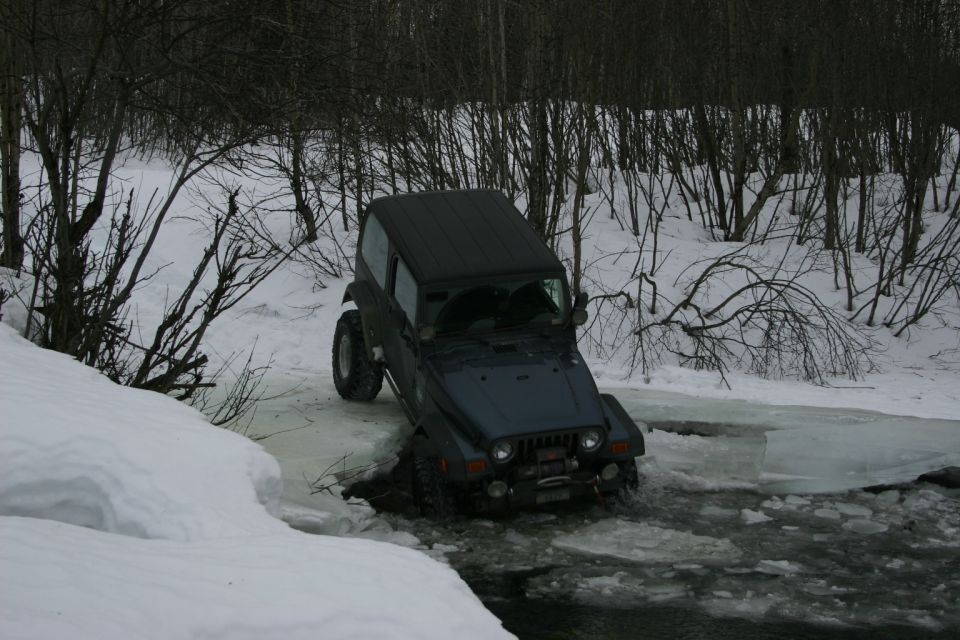 Dark blue Jeep Wrangler TJ crossing icy water with snow-covered banks