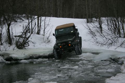 2003 Jeep TJ - 2003 Jeep TJ navigates a challenging icy water crossing in a snowy wooded area.