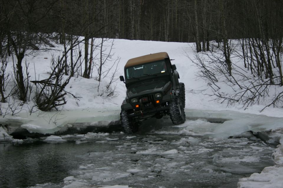 Green 2003 Jeep TJ with tan soft top driving through icy water and snow