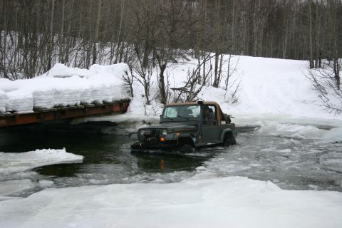 2003 Jeep TJ - A Jeep TJ navigates through icy water under a snow-laden bridge during winter.