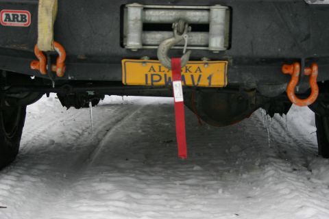 2003 Jeep TJ - A vehicle's rear bumper is equipped with a winch, tow hooks, and an Alaska license plate, seen in a snowy environment.