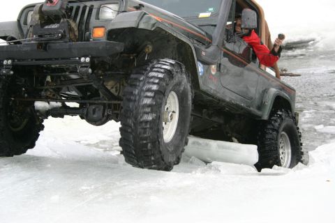 2003 Jeep TJ - A dark green 2003 Jeep TJ navigates icy terrain, its large tires gripping the frozen surface.