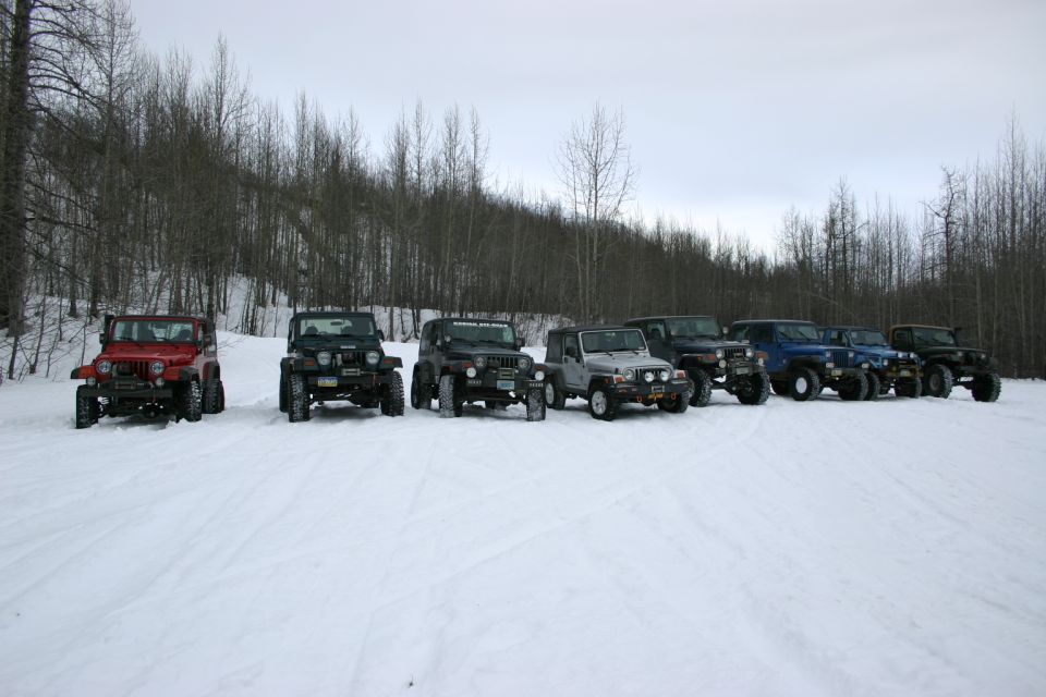Several Jeep TJs parked in the snow with trees in the background