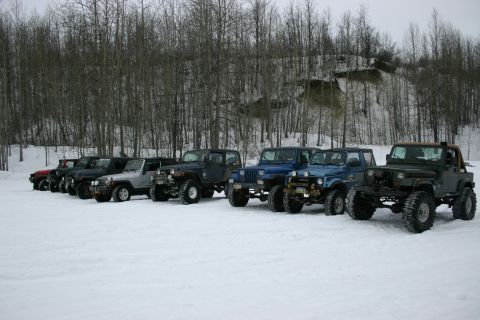 2003 Jeep TJ - Several Jeeps are parked in a snowy landscape with a forest and hill behind them.