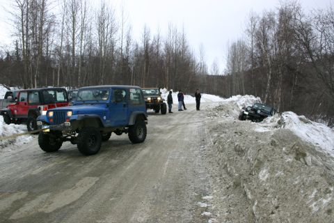 2003 Jeep TJ - A blue 2003 Jeep TJ is being towed on a snow-covered road, with several other Jeeps and people present in a winter scene.