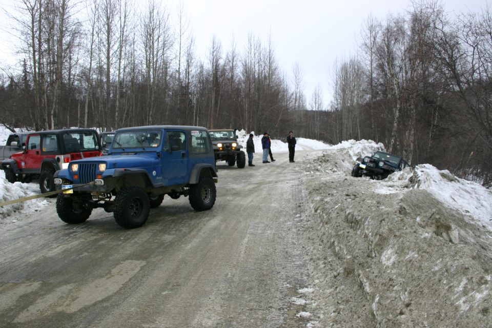 Blue 2003 Jeep TJ being towed on a snowy road with other Jeeps