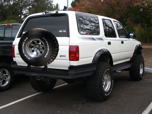 White lifted Toyota 4Runner with rear spare tire carrier and large BFGoodrich tires, rear three-quarter view