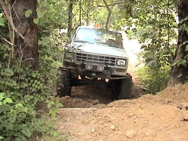 Light blue lifted Ford SUV climbing a dirt trail in the woods, front view