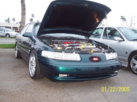 2002 Ford Taurus - A green sedan with its hood open reveals the engine bay, parked next to another vehicle.