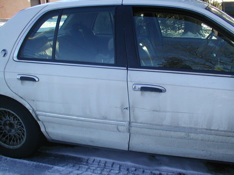 White sedan side view, dent on rear door, chrome trim, wire wheel