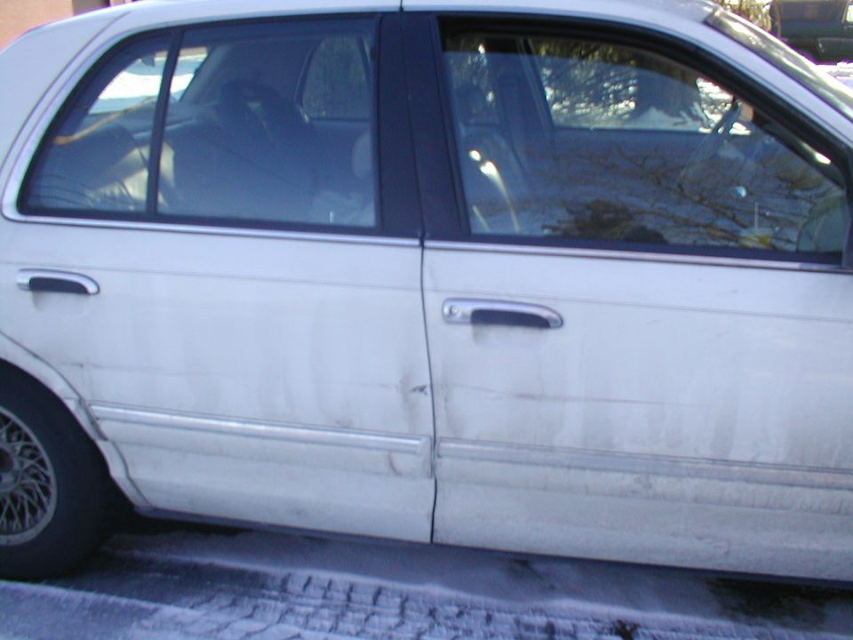 White sedan side view with dent on rear door