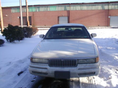 1979 Ford Bronco - A white sedan sits parked in a snowy lot in front of a brick building.