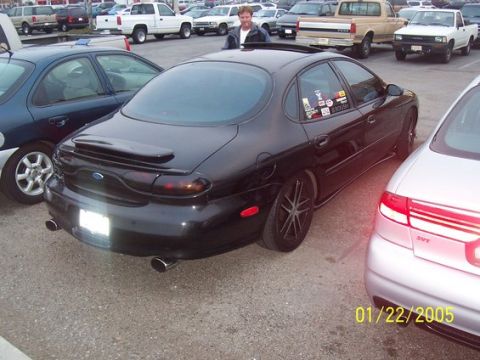 2002 Ford Taurus - A black 2002 Ford Taurus is seen from the rear in a parking lot with other vehicles.