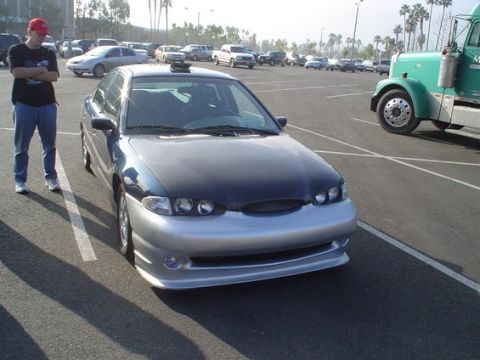 2002 Ford Taurus - Sedan with aftermarket front bumper and hood modification in a parking lot.