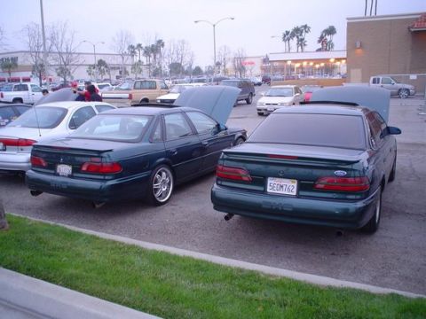 2002 Ford Taurus - Two dark green sedans are parked side-by-side in a parking lot, with one showing its license plate.