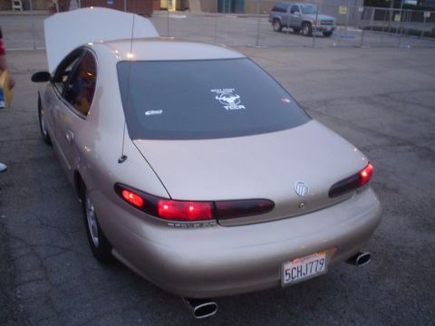 2002 Ford Taurus - A gold sedan is parked with its hood up, viewed from the rear, with another vehicle visible in the background.