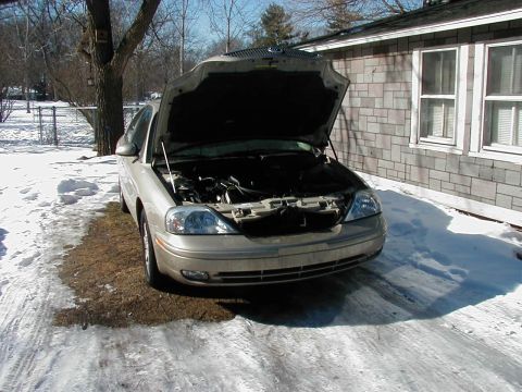2001 Mercury Sable - A tan sedan sits with its hood open on a snowy driveway, revealing the engine compartment.