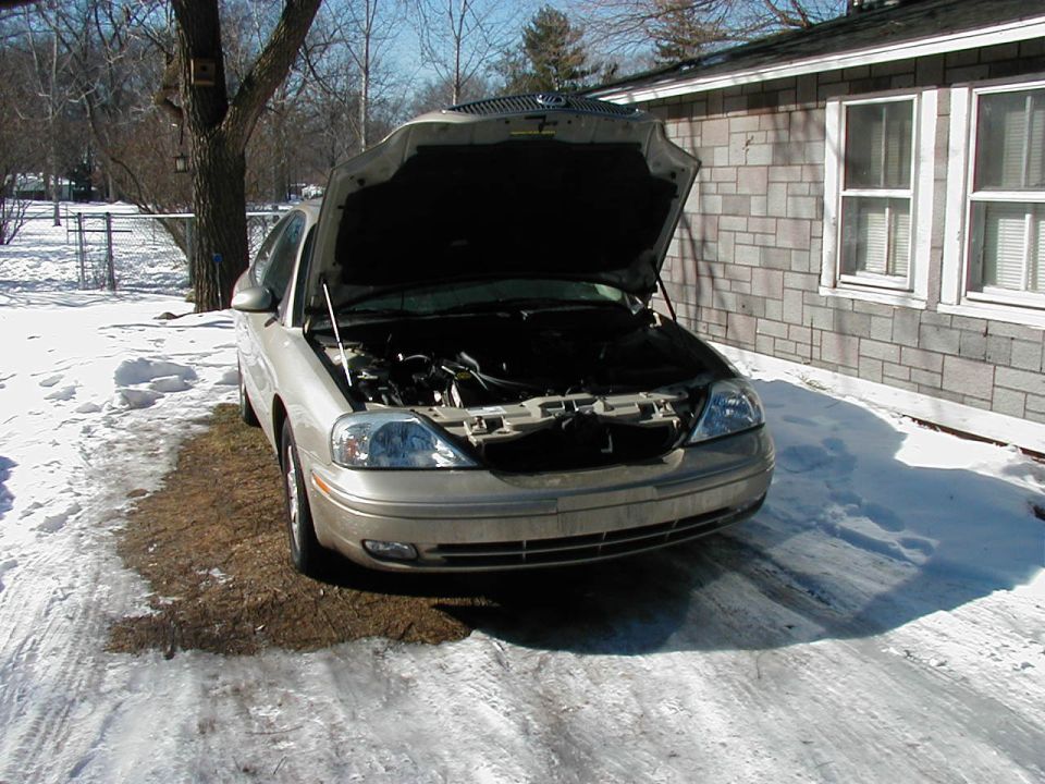 Tan sedan with hood open, parked on a snowy driveway