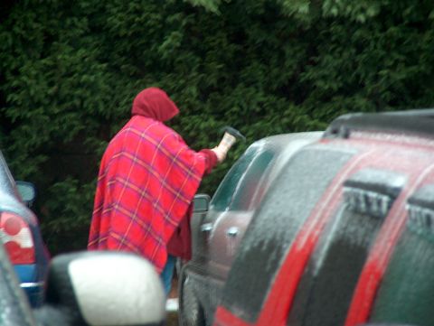 1998 Ford Taurus - Person in red plaid poncho cleans ice off car windshield in a parking lot.