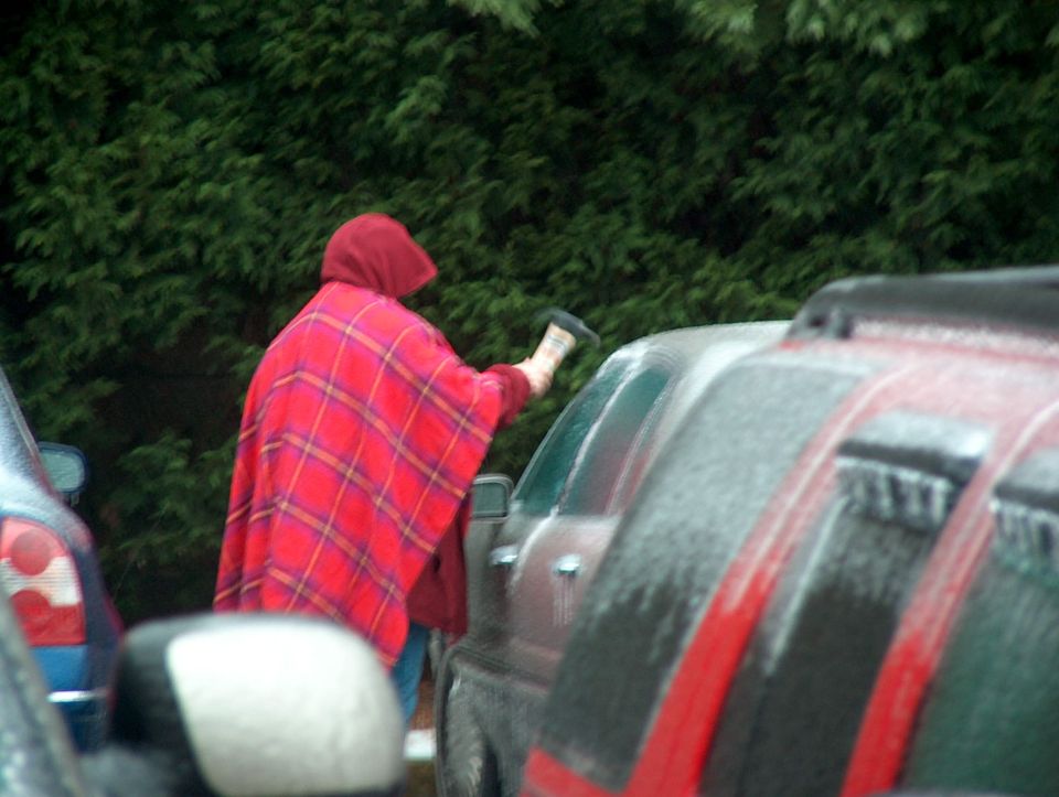 Person in red plaid poncho cleaning ice off car windshield