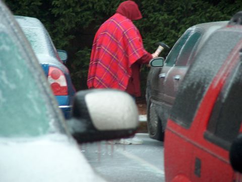 1998 Ford Taurus - A person dressed in a red plaid poncho appears to be preparing to strike an icy car with an axe.