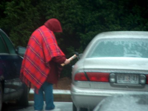 1998 Ford Taurus - A person in a red plaid poncho pumps gas into a silver 1998 Ford Taurus sedan in a parking lot.