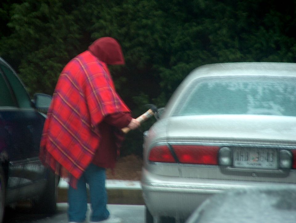 Silver 1998 Ford Taurus sedan rear view, license plate ARB 3543, with a person in a red plaid poncho at the gas pump