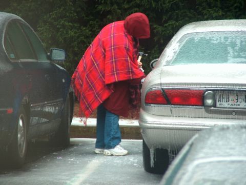 1998 Ford Taurus - Person in blanket with axe near a 1998 Ford Taurus covered in ice.