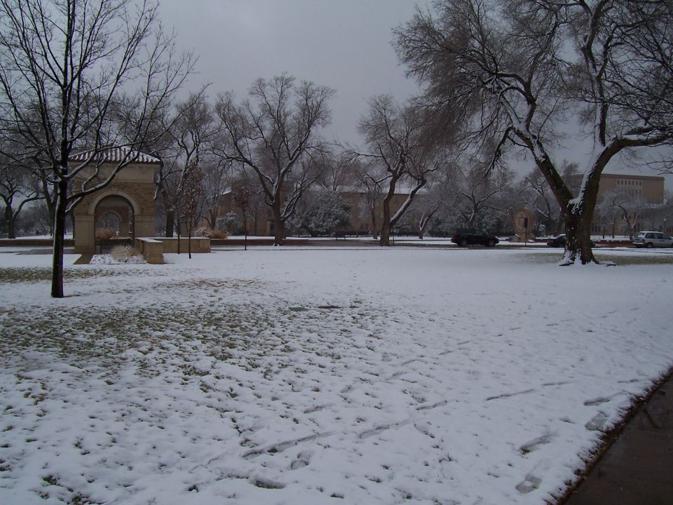 Snowy campus lawn with stone archway pavilion and bare trees under grey sky