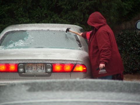 1998 Ford Taurus - A person scrapes ice off the rear window of a 1998 Ford Taurus, license plate AHB 3543 visible.