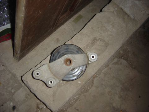 1998 Ford Taurus - A polished multi-groove crankshaft/underdrive pulley with a cast-metal bracket resting on top, set on a concrete garage floor beside a card…