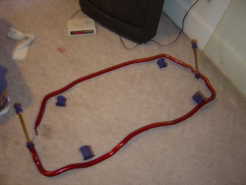 1998 Ford Taurus - A pair of red powder-coated anti-roll (sway) bars laid out on beige carpet indoors with purple polyurethane bushings and gold-anodized adju…