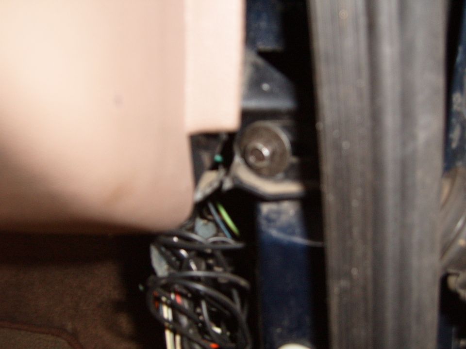 Close-up of blue door jamb hardware, weatherstrip and coiled wiring behind tan trim panel