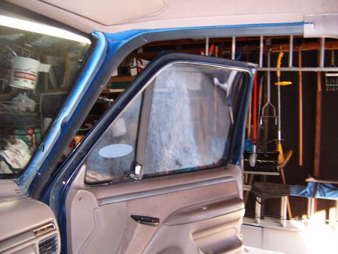1993 Ford Bronco - Open passenger door of a dark blue truck viewed from inside a garage, showing the tan door panel with power window switch and pull handle,…