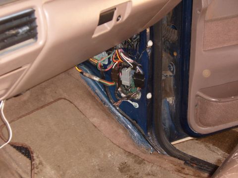 1993 Ford Bronco - Passenger-side kick panel removed on a tan-interior truck, exposing the door-jamb wiring harness with white and black multi-pin connectors…