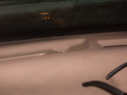 1993 Ford Bronco - Dim close-up looking down at a tan interior trim panel with a screw boss and a small tan plastic clip lying on it, with dark tinted glass a…