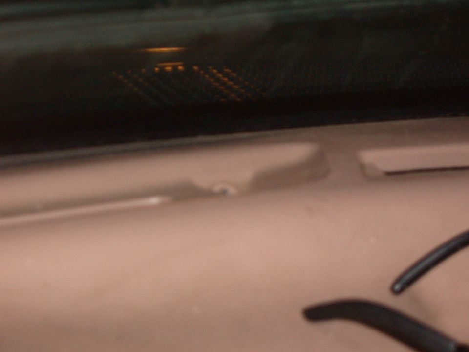 Close-up of tan interior trim panel with a loose clip below tinted defroster glass